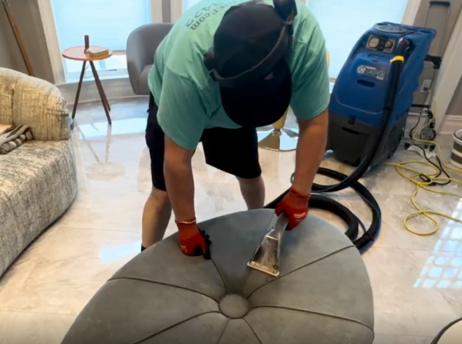 Professional house cleaner expertly steam-cleaning a fabric ottoman, restoring freshness and removing stains using eco-safe methods.
