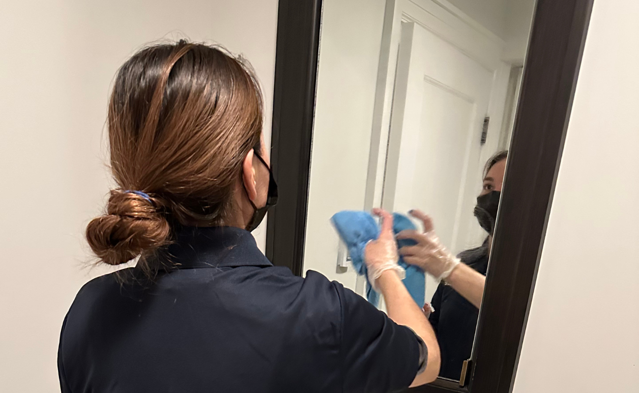 Professional maid cleaning bathroom mirror with streak-free glass cleaner for spotless shine